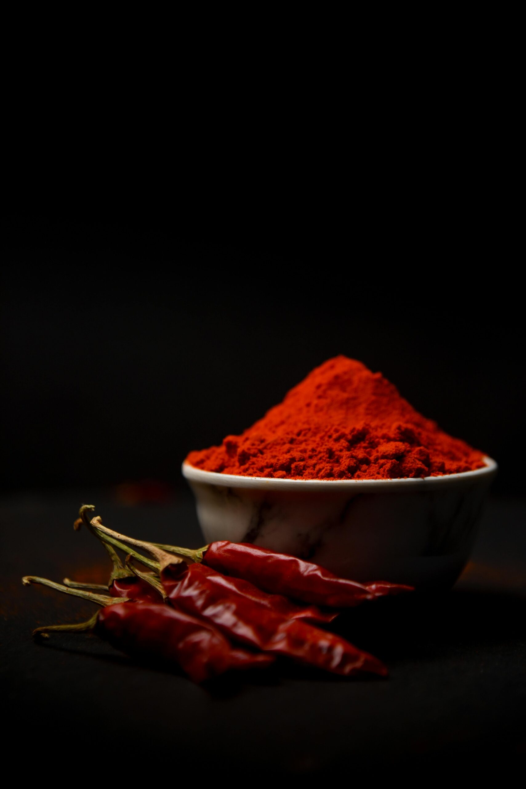 Rich red chili powder and whole chilies in stark contrast against a dark backdrop.
