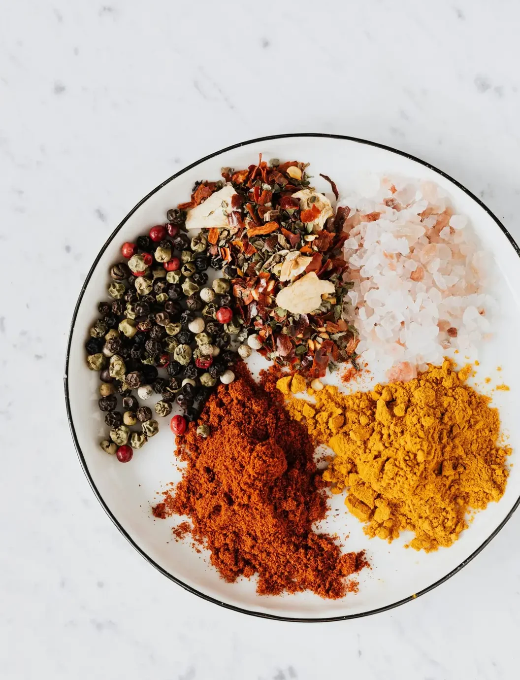 From above of bowl filled with piled of turmeric and paprika powder near mix of pepper flakes and seeds with sea salt on table