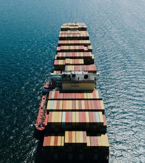 Drone shot of a loaded container ship sailing through the sea near Naples, Italy.